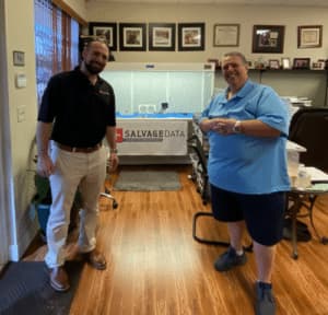 Two men standing in front of a sign that says salvaged data.