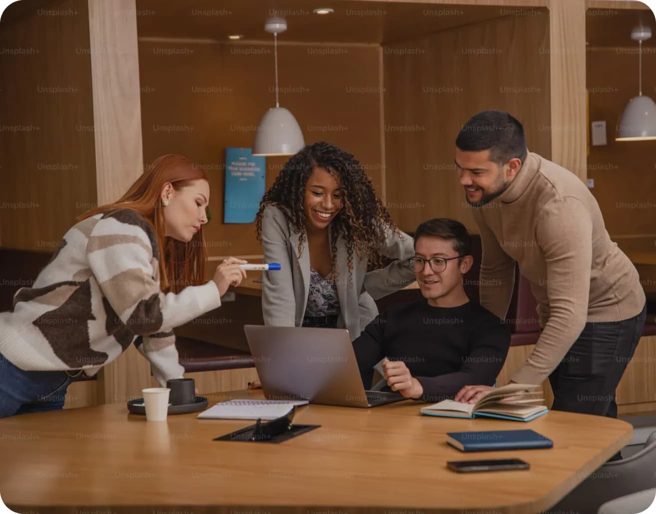 A group of people are gathered around a table with a laptop.
