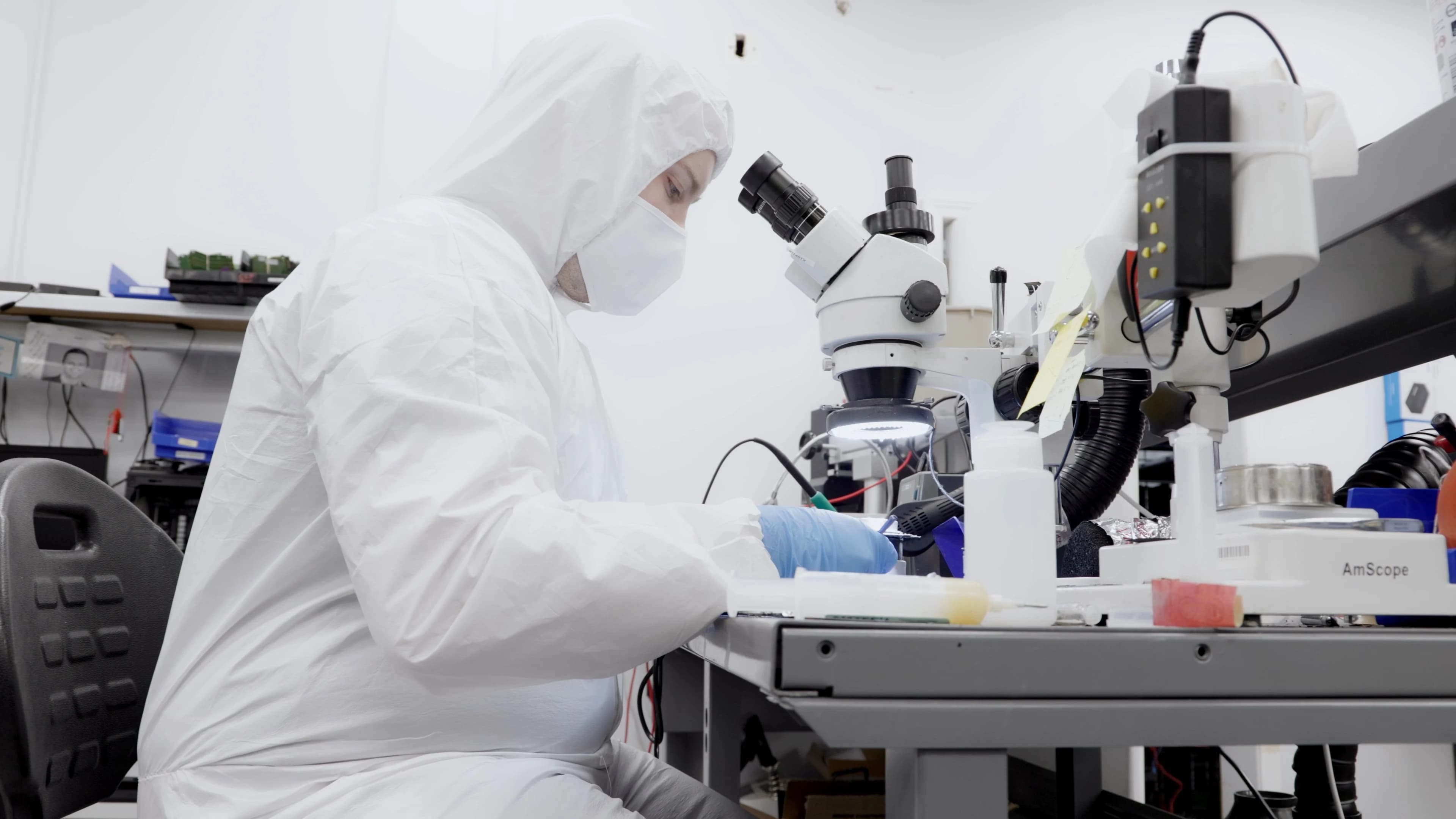 A man wearing a white lab coat is working at a microscope.