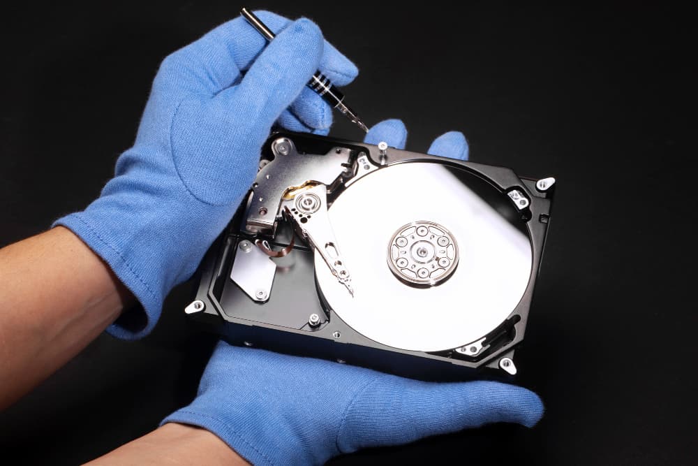 A person wearing blue gloves is holding a computer hard drive.